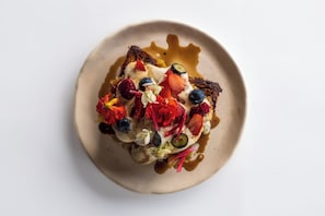 A plate with toast topped with cream, strawberries, blueberries, and other fruits.