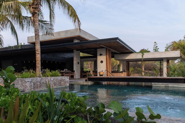 Un edificio moderno con piscina, rodeado de vegetación exuberante y palmeras.
