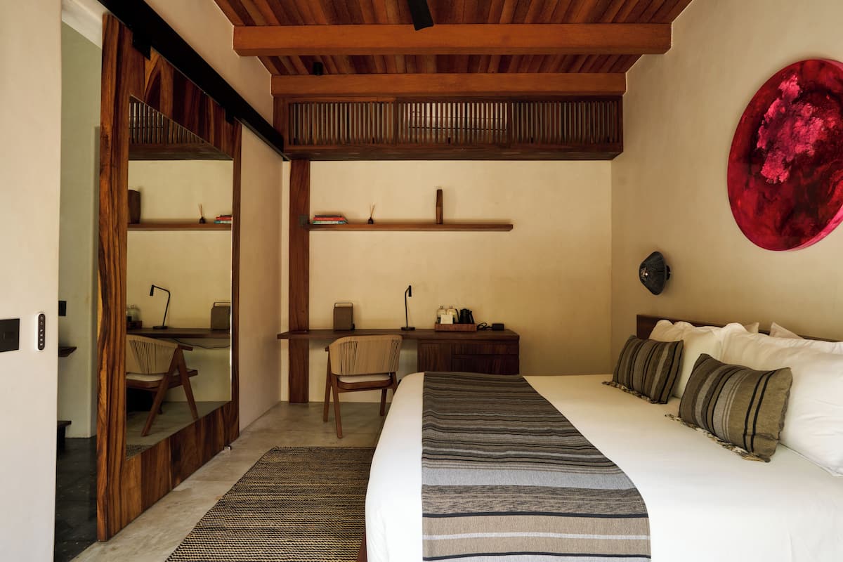 A bedroom with a bed, a desk, a chair, a large mirror, and a red abstract art piece on the wall.