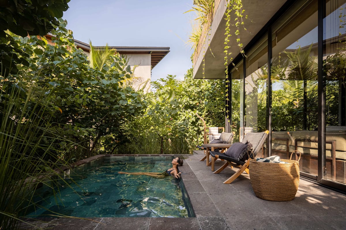 A swimming pool with clear water, surrounded by lush greenery and modern outdoor furniture.