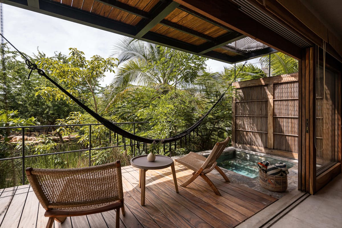 A wooden deck with a hammock, two wicker chairs, a small round table, and a hot tub.