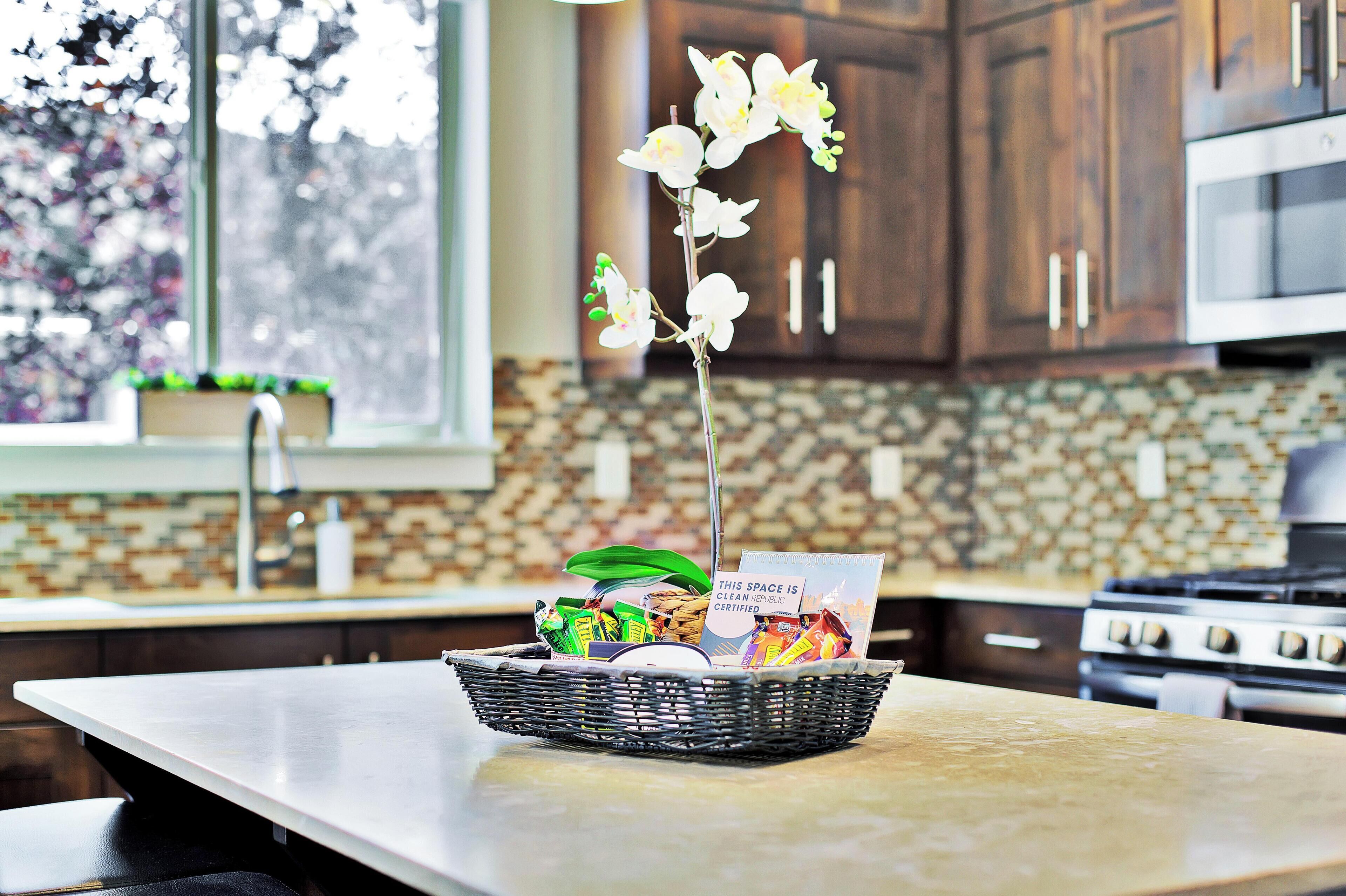 A kitchen with a stone backsplash, wooden cabinets, a stainless steel microwave, and a basket with a card on the counter.