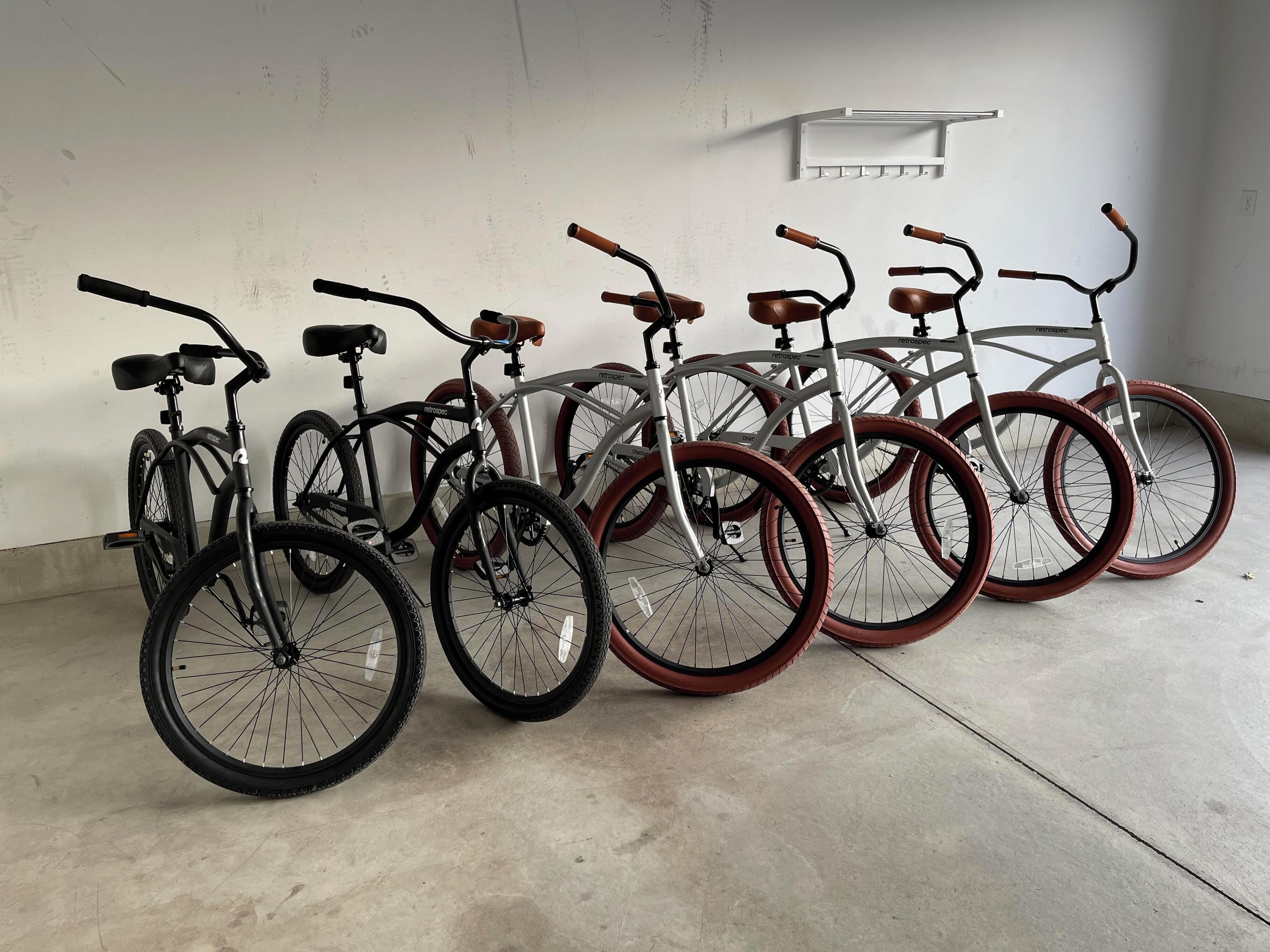 A row of bicycles with different wheel colors and handlebars, parked indoors against a plain wall.