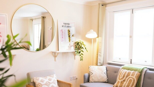 Una sala de estar con un sofá gris, un espejo redondo, una mesita con una planta y un estante de pared con un cuadro enmarcado.