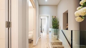 A modern hallway with a glass railing, a staircase, and a potted plant.