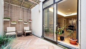 A modern patio with wooden slats, two cushioned chairs, and potted plants.