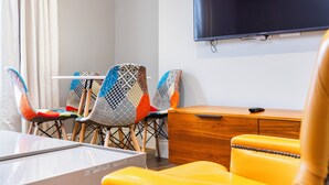 Una moderna camera d'albergo con una scrivania in legno, una televisione a parete e sedie colorate.