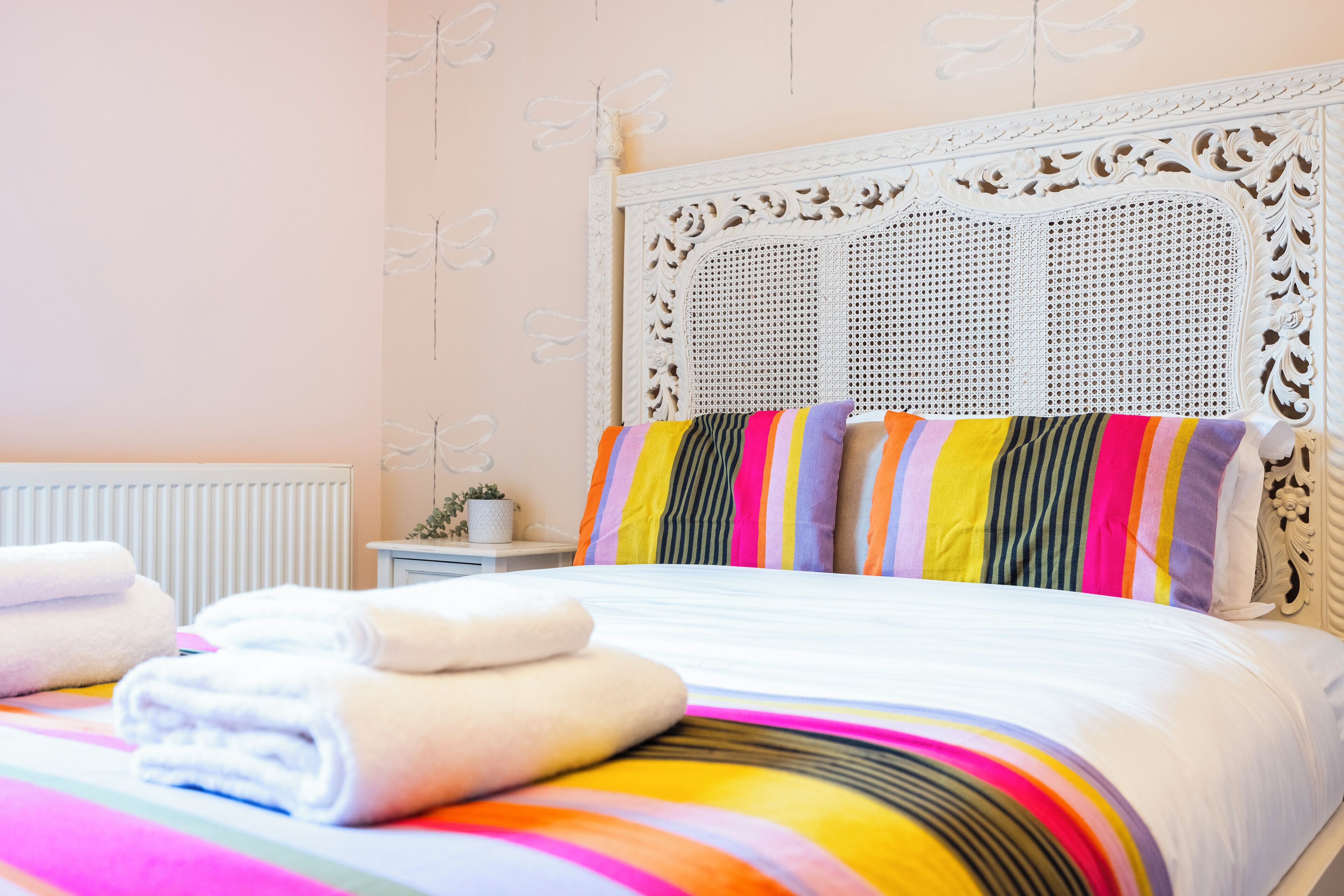 A neatly made bed with colorful striped bedding, a white ornate headboard, and neatly folded towels on the side.
