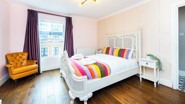 Una camera da letto con un letto bianco, una sedia di legno, un comodino bianco e una finestra con tende.