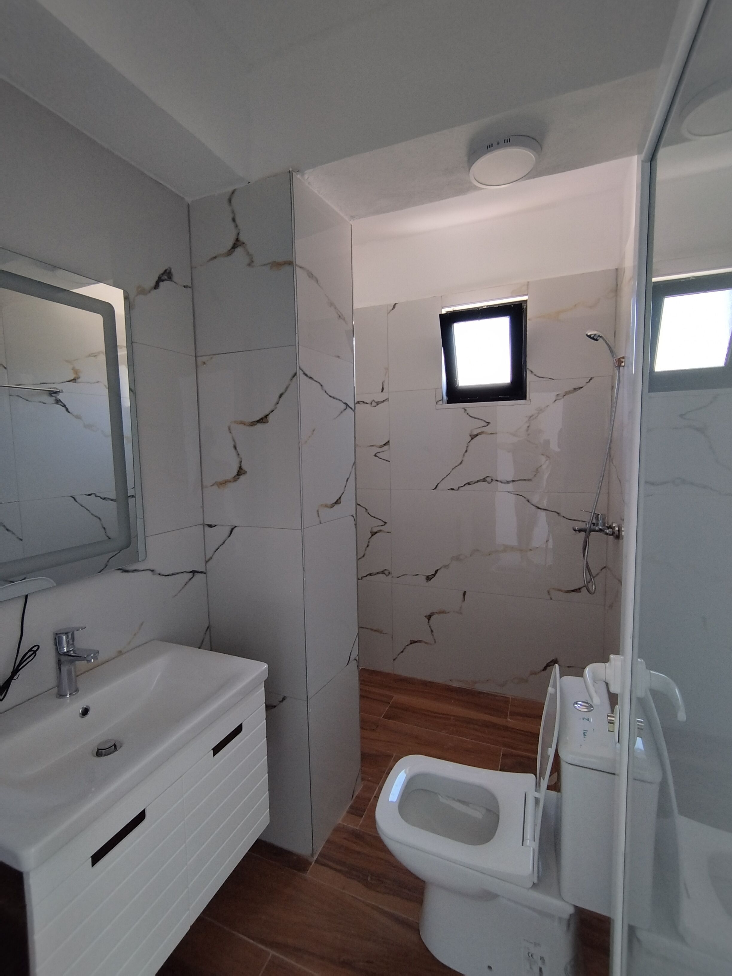 A bathroom with a marble wall, a sink, a toilet, and a shower.