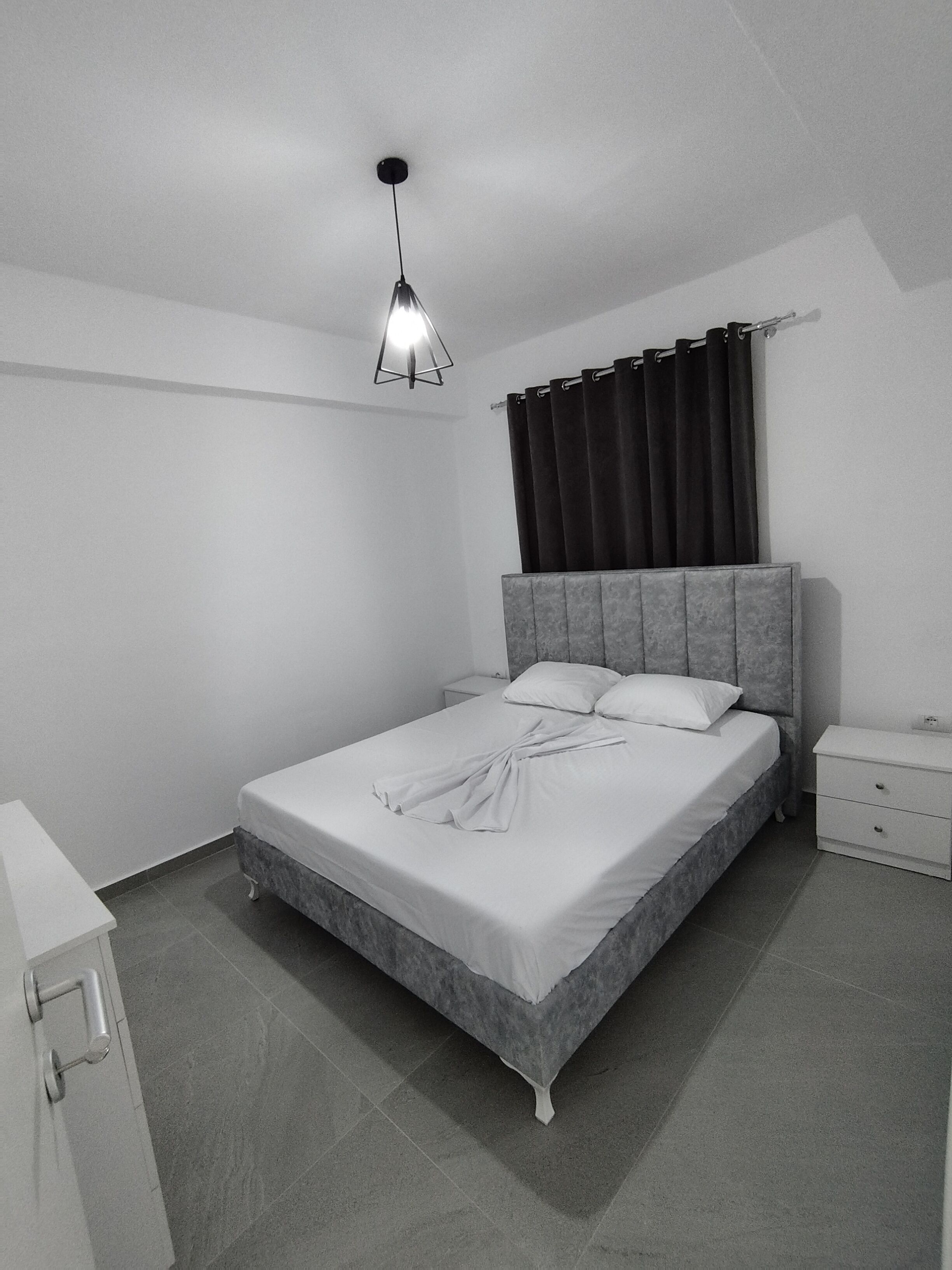 A bedroom with a bed, nightstand, and a hanging light fixture.