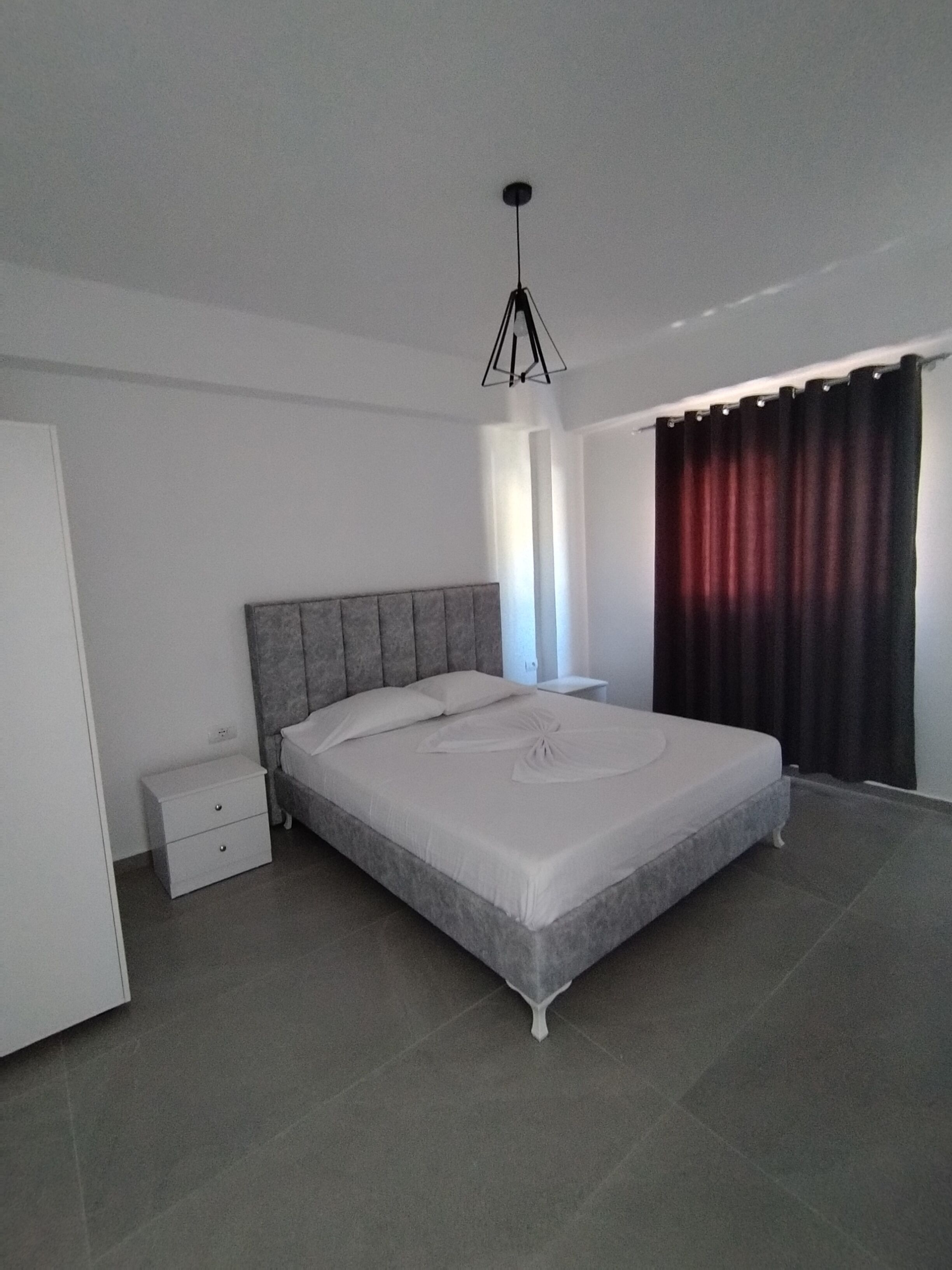 A modern bedroom with a large bed, a bedside table, a wardrobe, and a hanging light fixture.