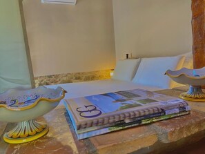 A bed with white linens, a decorative bowl, and a stack of books on a stone surface. - Casolare Maestrale  (Perugia)