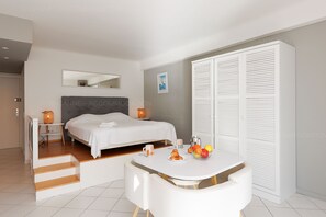 Une chambre d’hôtel avec un lit, une table de chevet, une lampe de chevet, une armoire blanche et une petite table où est disposé le petit-déjeuner.