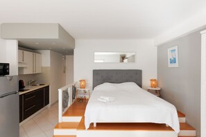 Une chambre d’hôtel moderne équipée d’un lit, de tables de chevet, d’un petit coin cuisine et d’un miroir.
