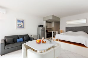 Una habitación de hotel moderna con cama, sofá, mesa de comedor con desayuno, área de cocina y un cartel en la pared.