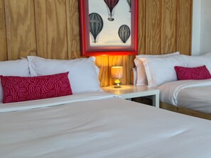 Een hotelkamer met twee bedden, een nachtkastje met een lamp en een lijst met luchtballonnen aan de muur.