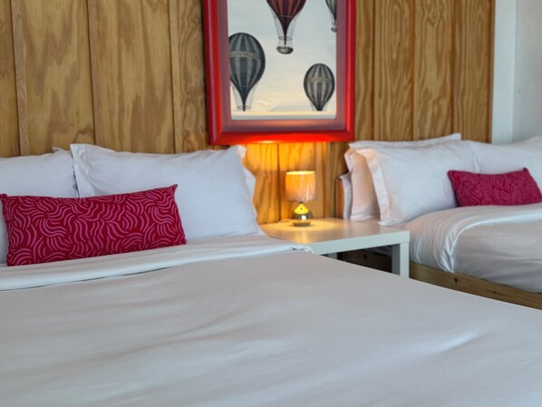 A hotel room with two beds, a nightstand with a lamp, and a framed picture of hot air balloons on the wall.