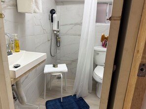 Een badkamer met douche, toilet, wastafel en een klein krukje.