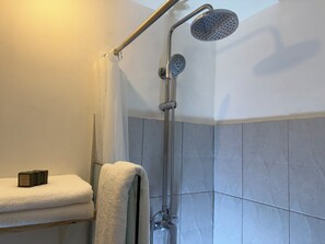 Suihkussa on käsisuihkupää ja seinään kiinnitetty sadesuihkupää, pyyheteline, jossa on pyyhe, sekä pieni hylly, jossa on kirja.