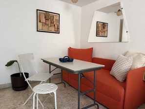 A room with a white table, orange sofa, a small white chair, a potted plant, and two framed wooden art pieces on the wall.