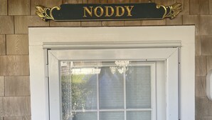 Fachada de madera con un letrero que dice "NODDY" sobre un ventanal con marco blanco.
