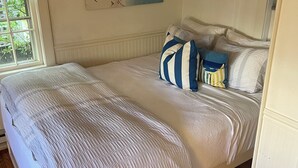 Una cama bien hecha con un almohadón a rayas, una ventana con persianas y un aire acondicionado de pared.