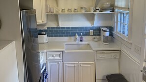 Cocina compacta con armarios blancos, un refrigerador de acero inoxidable, lavavajillas y piso de madera.