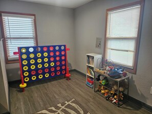 Une pièce avec un panneau perforé bleu et rouge, une bibliothèque remplie de jouets et un tapis à motifs.