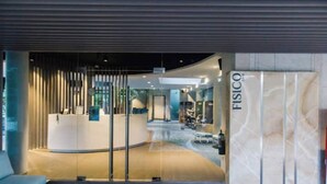 A modern reception area with a curved desk, a reception counter, and a glass door leading to a lobby with seating and a reception desk. - The Pearl of Mactan (Lapu-Lapu City)