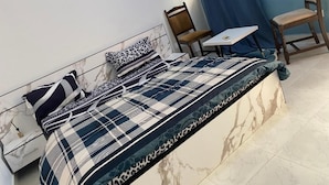 A bed with a checkered bedspread, a marble headboard, and a small table with a chair beside it. - RESIDENCE EL HADJI (Dakar)