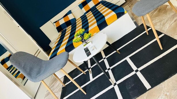 A modern room with a checkered bedspread, a round white table, and two grey chairs. - RESIDENCE EL HADJI (Dakar)