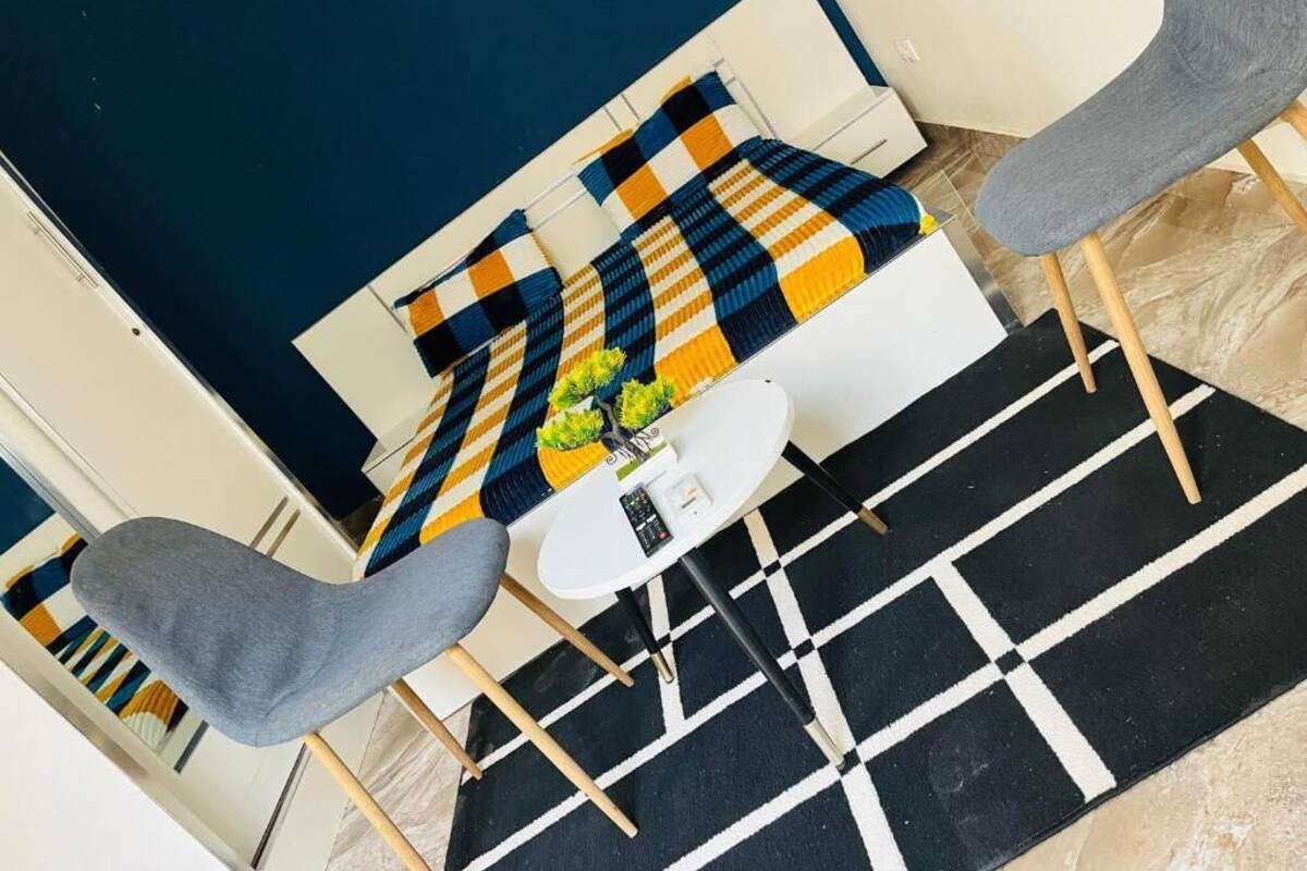 A modern room with a checkered bedspread, a round white table, and two grey chairs.