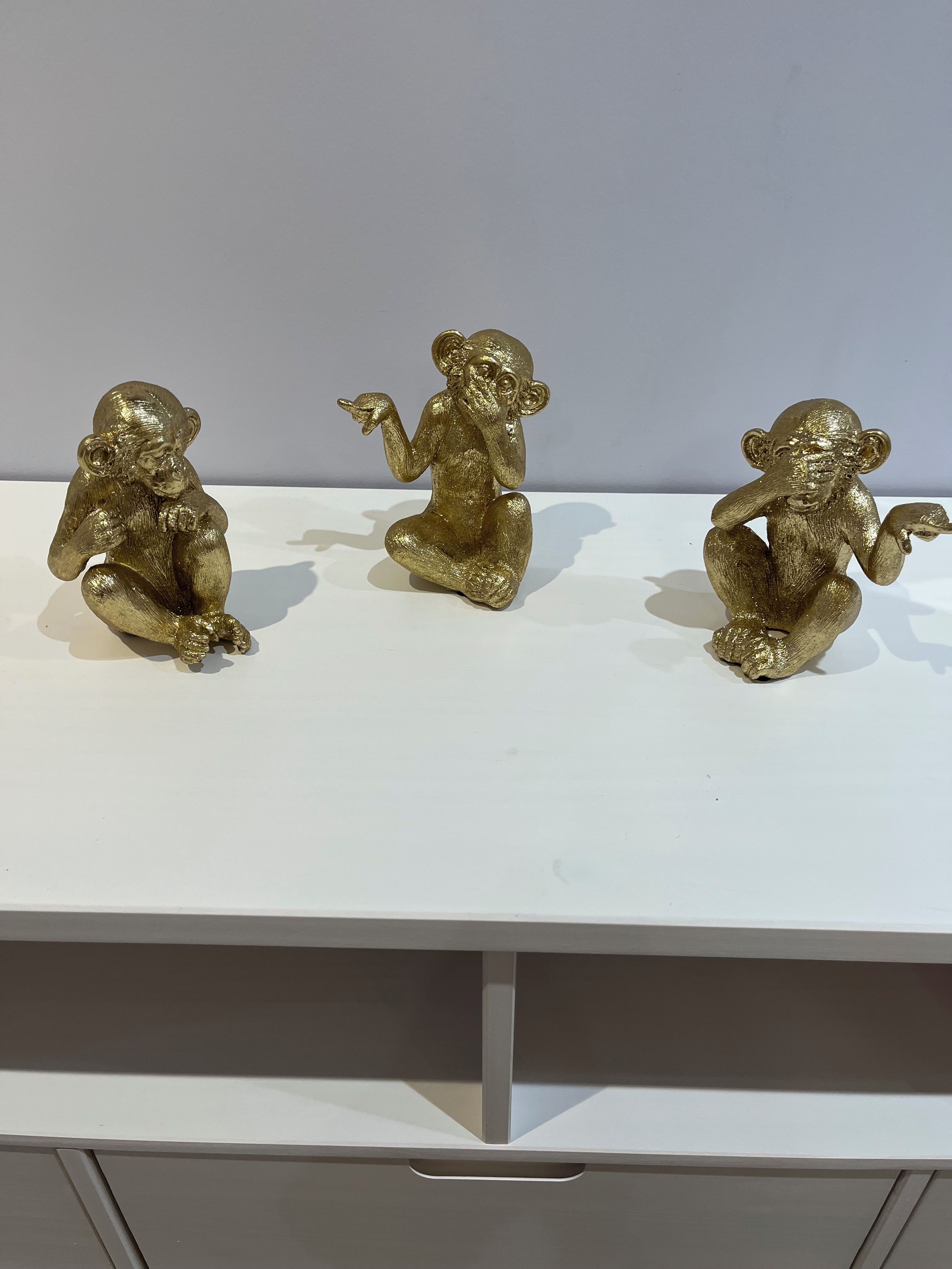 Three golden monkey figurines on a white shelf.