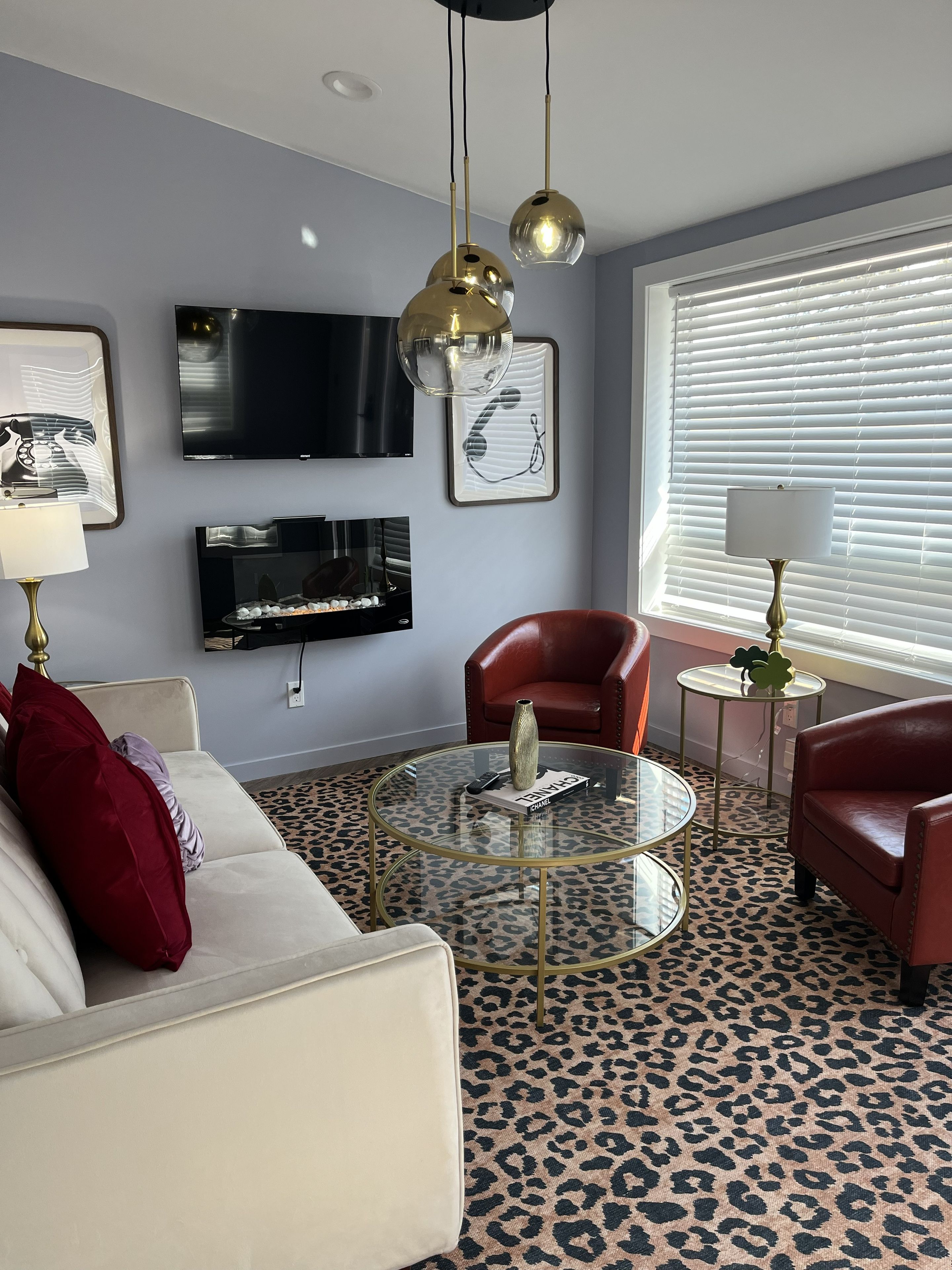 A living room with a white sofa, red armchair, glass coffee table, and a flat-screen TV mounted on the wall.