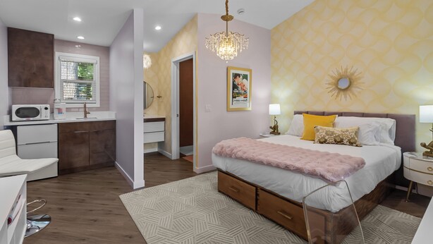 A modern bedroom with a large bed, bedside tables, a chandelier, and a bathroom visible through an open door.