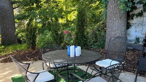 A patio with a round table and four chairs, surrounded by trees and greenery.