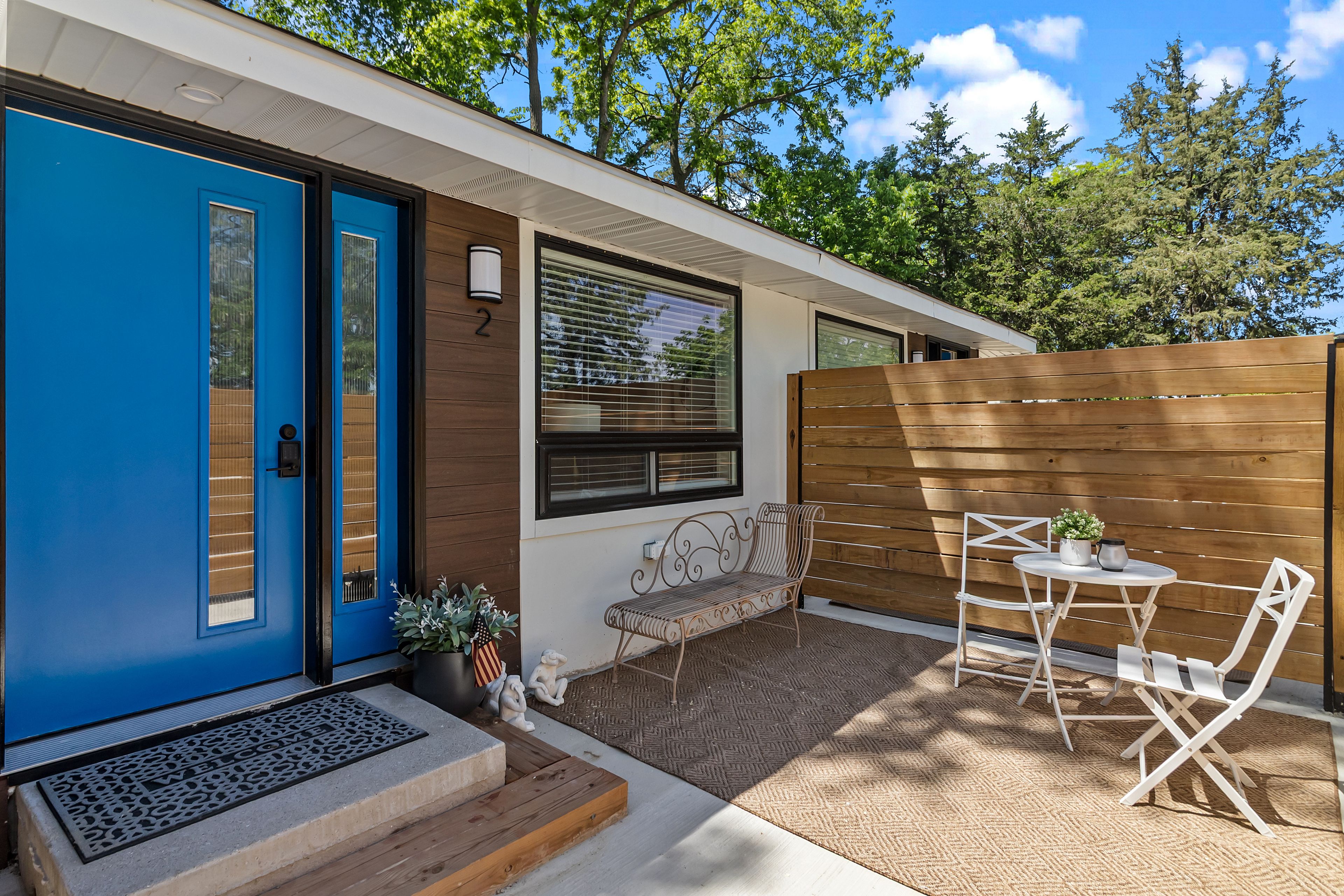 A residential property with a blue door, a wooden fence, a bench, and a table with chairs.