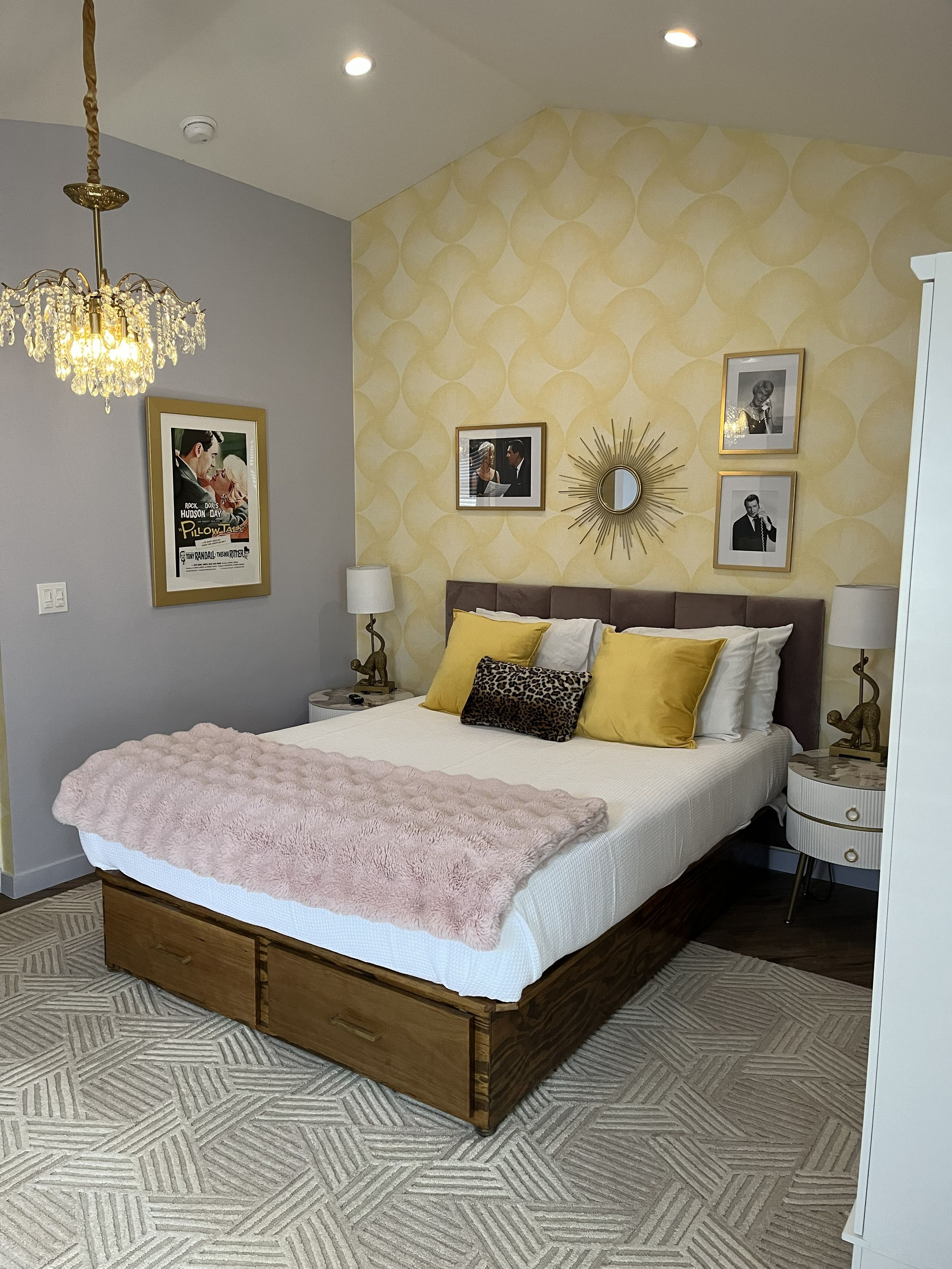 A bedroom with a bed, a chandelier, a patterned wall, and framed pictures.