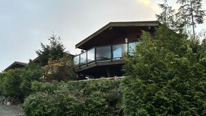 Un bâtiment moderne doté d’un balcon en verre, entouré d’une végétation luxuriante.
