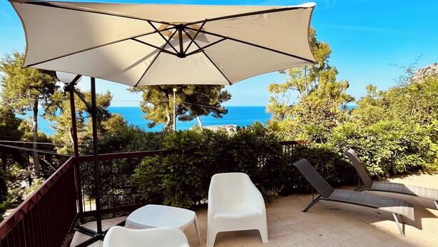 An outdoor seating area with a large umbrella, two white chairs, and a table, overlooking a scenic view. - Porta Addaura (Palermo)