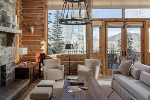A log cabin interior with a fireplace, seating area, and a view of snow-covered mountains.