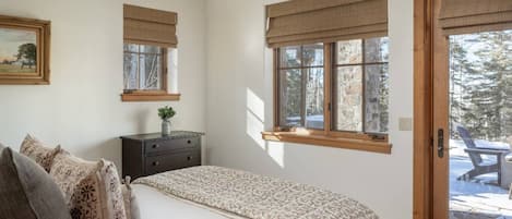 A bedroom with a bed, dresser, and windows with blinds.