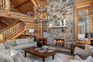 A log cabin interior with a stone fireplace, a staircase, and a cozy seating area. - Bear Lodge - Luxurious log home with ski-in/out! (Mountain Village)