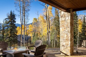 A covered outdoor seating area with chairs and a table, surrounded by trees and a stone wall.