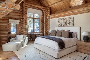 A log cabin bedroom with a large bed, a desk, and a chair.