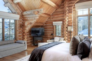 A log cabin interior with a large bed, a television, and a sofa.