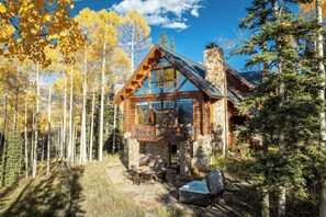 A log cabin with a stone chimney, a deck with outdoor seating, and a stone patio.