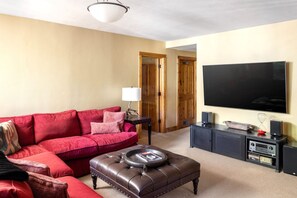 A living room with a red sofa, a brown ottoman, a TV, and a sound system. - Bear Lodge - Luxurious log home with ski-in/out! (Mountain Village)