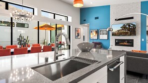 Una cocina moderna con una isla central, horno empotrado y comedor con sillas naranjas.